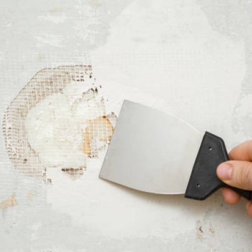Plaster Repairs Canberra4 Young adult man hand using spatula and plastering concrete wall hole with putty on mesh. Closeup. Repair work of home. Renovation process.